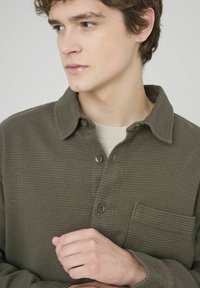 Chemise olive verte à manches longues en tissu texturé et côtelé, dotée d'une poche poitrine et d'un col.