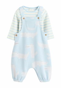 Lichtblauwe overall met witte krokodilpatronen, voorzien van een voorzak en houten knopen. Gestreepte blouse met lange mouwen in lichtblauw en wit.