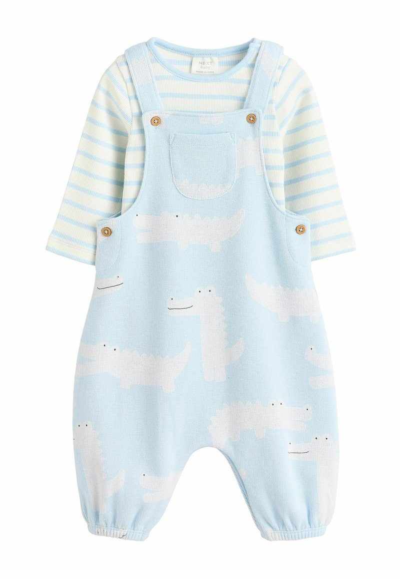 Lichtblauwe overall met witte krokodilpatronen, voorzien van een voorzak en houten knopen. Gestreepte blouse met lange mouwen in lichtblauw en wit.