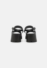 Sandales noires à plateforme avec deux brides croisées, une bride ajustable à la cheville, et un talon en bloc texturé présentant des découpes.