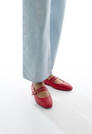 Chaussures Mary Jane en cuir rouge avec un bout arrondi, deux fines lanières avec des boucles dorées, associées à un jean fluide bleu clair.