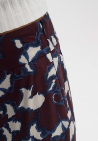 Détail de la taille d'une jupe à motifs floraux abstraits bleu, blanc et bordeaux avec fermeture éclair latérale et poche, portée avec un haut blanc côtelé.