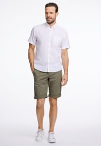 Vit kortärmad skjorta med knappar och bröstficka, ihop med olivgröna shorts och vita sneakers. Enkel design, lätt material.
