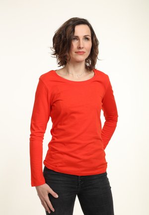 Rode katoenen t-shirt met lange mouwen en een ronde halslijn, gedragen met donkere jeans. Eenvoudig, passend ontwerp zonder zichtbare patronen of versieringen.