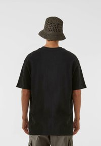 Črna prevelika majica s kratkimi rokavi, bombažna tkanina, kombinirana s temno sivo kvačkasto klobukom v slogu vedra z odprto tkanino.