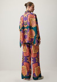 Színes, mintás, sima anyagból készült kétrészes öltözet; nagy virágos és absztrakt minták díszítik narancs, lila és zöld árnyalatokban.