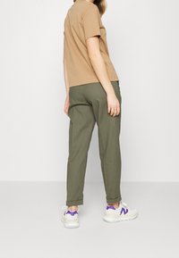 Krátký rukáv oranžového trička v kombinaci s volnými olivovými kalhotami a bílými teniskami s fialovými akcenty. Jednoduchý, ležérní design.