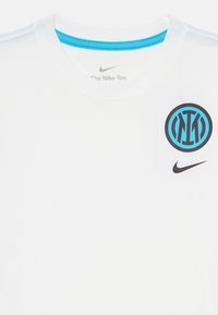 T-shirt en coton blanc avec un logo circulaire bleu et noir sur le côté gauche de la poitrine et un petit logo Nike noir en bas à droite.