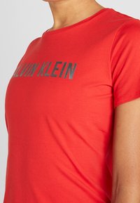 Rød bomulds T-shirt med rund hals og korte ærmer, prydet med et fremtrædende gråt "CALVIN KLEIN" logo på brystet.
