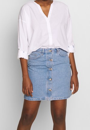 Blouse en coton blanc avec un décolleté en V et des manches retroussées, associée à une jupe en denim bleu clair avec une fermeture à boutons sur le devant.