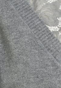 Tissu tricoté gris doux avec des détails bord-côtes couvrant partiellement une délicate superposition de dentelle florale dans une teinte grise assortie.