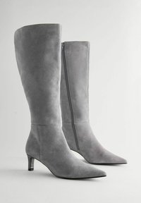 Botas altas de ante gris hasta la rodilla con punta afilada, cremallera en el lado interior y un tacón bajo y delgado. Textura suave y diseño elegante.