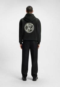 Felpa nera con un grande grafico circolare sul retro, caratterizzato da un design bianco. Abbinata a pantaloni neri larghi e scarpe nere.
