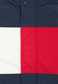 Μπουφάν με χρωματικά μπλοκ σε ναυτικό μπλε, κ όκκινο και λευκό. Διαθέτει κλείσιμο με κουμπιά και ομαλή υφή υφάσματος. Απλός, μοντέρνος σχεδιασμός.