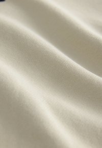 Cremefarbener Stoff mit einer glatten, leicht strukturierten Oberfläche, die Licht reflektiert; sichtbare Webmuster und weiche Falten.