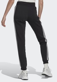 Pantaloni tuta neri con righe laterali bianche, vita elastica e polsini alla caviglia affusolati, realizzati in un materiale morbido e flessibile.