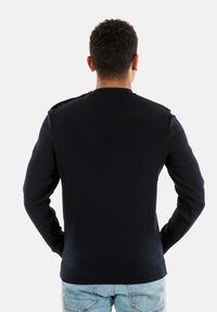 Maglione blu navy lavorato a maglia con colletto rotondo, maniche lunghe e orlo a coste. La vista laterale mostra una texture liscia e un design aderente.