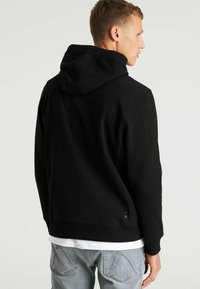 Sudadera con capucha negra hecha de una mezcla de algodón, presenta un corte relajado, puños acanalados y un sutil detalle del logo cerca del dobladillo.