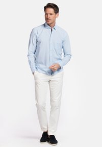 Lichtblauwe overhemdbloes met een zachte textuur, een enkele borstzak, gecombineerd met witte broek en zwarte instappers.
