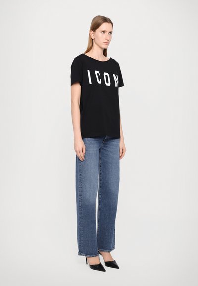 T-shirt en coton noir avec "ICON" en lettres blanches, associé à un jean en denim bleu taille haute et des chaussures noires à bout pointu.