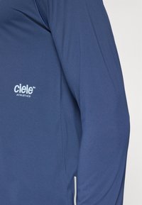 Navy athletic long-sleeve top with a smooth texture. Features a white "ciele Athletics" logo on the chest and contrasting accents.