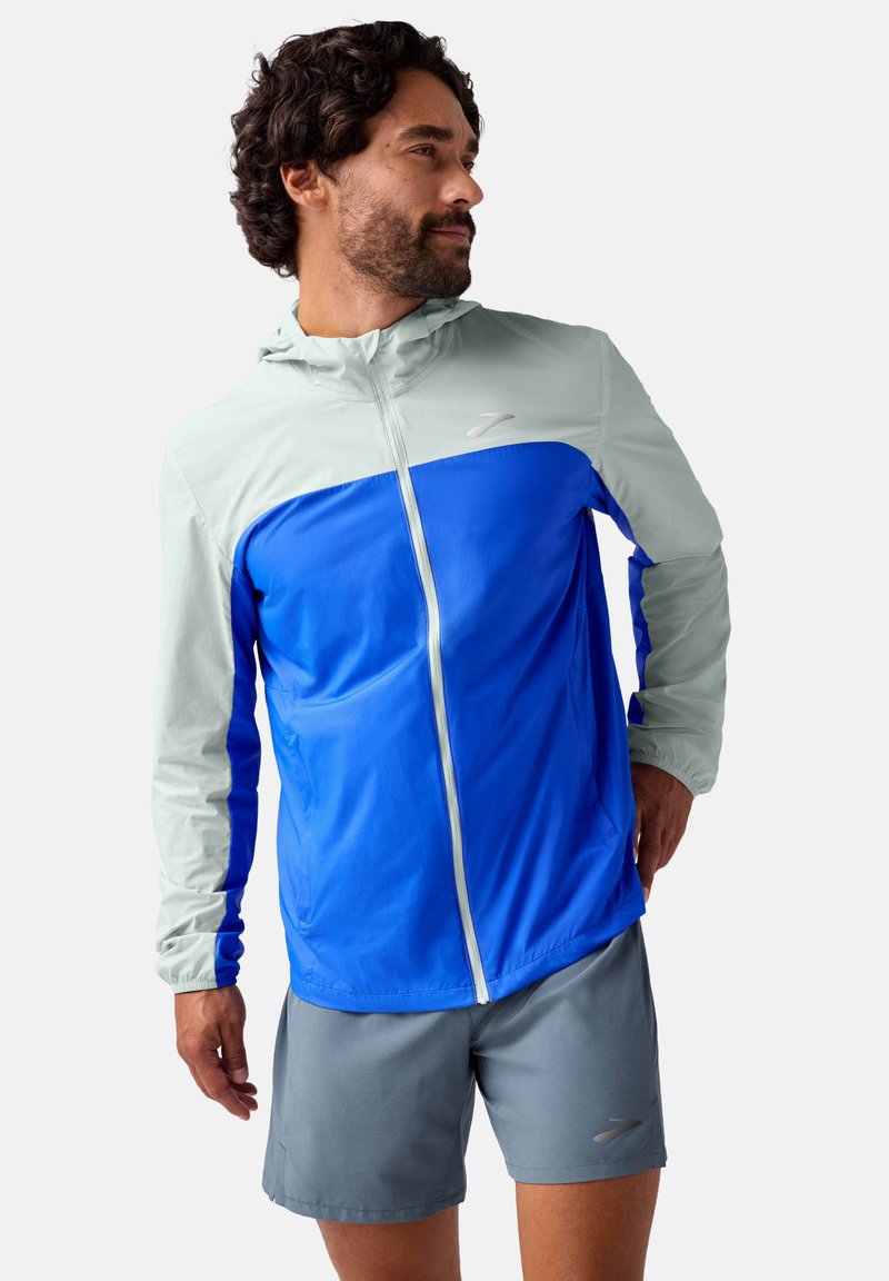 Leichte Laufjacke in Blau und Hellgrau, ausgestattet mit einer Kapuze, durchgehendem Reißverschluss und elastischen Bündchen. Glattes Material mit atmungsaktivem Design.