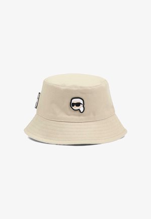 Beżowy kapelusz typu bucket z małą haftowaną kreskówkową twarzą w okularach przeciwsłonecznych i białą chustą na głowie, umieszczoną na środku z przodu.