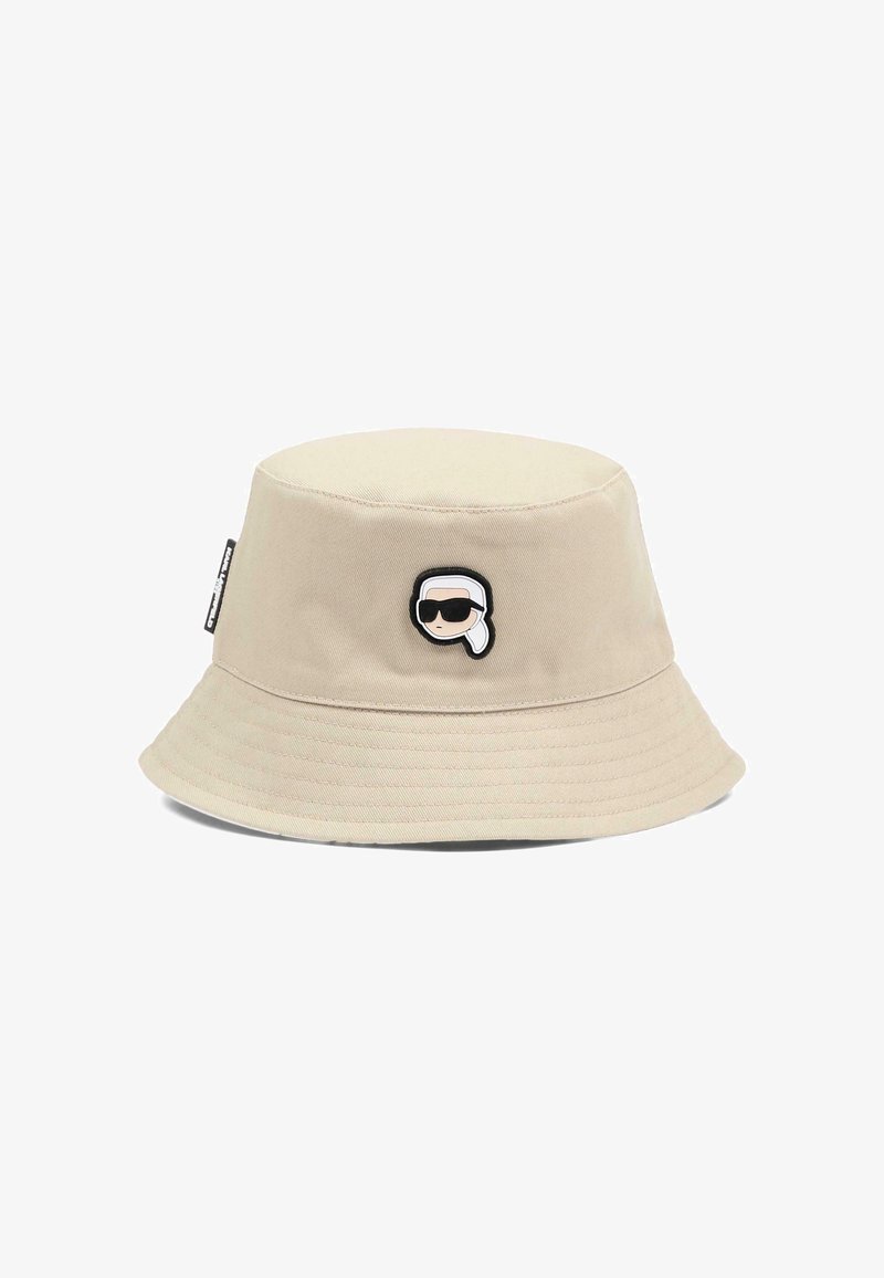 Beżowy kapelusz typu bucket z małą haftowaną kreskówkową twarzą w okularach przeciwsłonecznych i białą chustą na głowie, umieszczoną na środku z przodu.