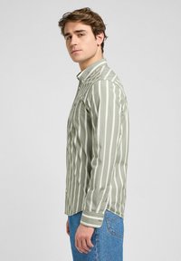 Camicia a maniche lunghe a righe verde e bianca, con colletto e taschino sul petto, dal taglio dritto e polsini abbottonati.