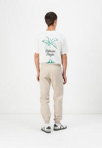 White t-shirt with green palm tree graphic and text "Palmeira Paraíso," beige elastic waistband pants, and black and white sneakers.