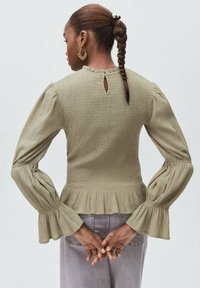 Olivno zelen peplum top z nabranim povočem, dolgimi napihnjenimi rokavi in detajlom odprtine na hrbtu. Mehka tekstura in razširjeni manšeti na rokavih.