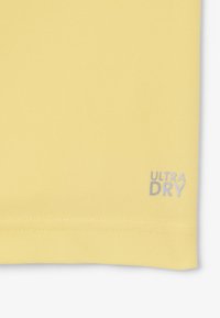 Tessuto di una polo gialla con una finitura texturizzata. Presenta un logo grigio "ULTRA DRY" sul lato. Orlo dritto con cuciture ordinate.