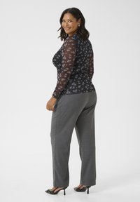 Haut à manches longues noir avec motif floral, associé à un pantalon gris. Les manches transparentes ajoutent de la texture. Fini avec des chaussures à talons hauts noires.