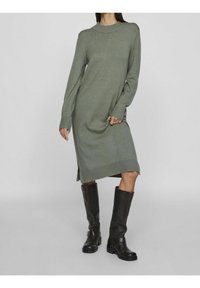 Knit, long-sleeve dress in muted green with a crew neckline, side slits, and ribbed cuffs. Paired with tall black leather boots.