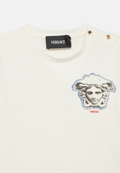 Λευκό βαμβακερό T-shirt με γραφικό έμβλημα της Μέδουσας σε γκρι και μπλε, με χρυ σά κουμπιά στο ώμο. Ετικέτα: Versace.