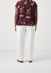 Bordeaux bloemen blouse met korte mouwen en een ronde hals, gecombineerd met witte wijde broeken en zwarte platte sandalen.