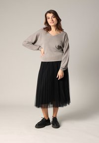 Haut en V à manches longues de couleur gris métallique léger, associé à une jupe en tulle plissé noire et à des chaussures à lacets noires. Texture plate et design superposé.