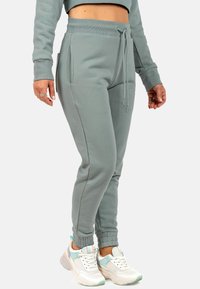 Lichtgrijze sweatpants hebben een elastische tailleband met een trekkoord, zijzakken en ribgebreide boorden, gecombineerd met witte en pastelkleurige sneakers.