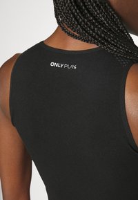 Czarny sportowy top na ramiączkach o dopasowanym kroju, gładkiej fakturze i białym logo "ONLY PLAY" na plecach.