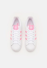White sneakers with pink stripes, textured leather upper, round rubber toe cap, flat white laces, and branded tongue and insole.