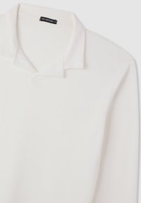Polo bianco con una texture a coste, dotato di colletto piegato e un'etichetta che recita 'Terranova XL'.