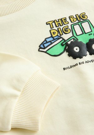 Krämfärgad sweatshirt med ett motiv av en grön tipptruck med blått material. Ribbstickade muddar, rund halsringning och strukturerat tyg.