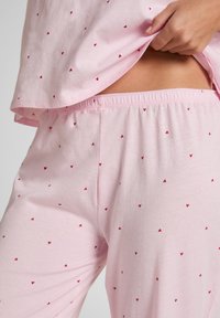 Rosa Pyjama-Set aus weichem Stoff mit lockerem Oberteil und Hosen mit elastischem Bund, verziert mit kleinen roten Herzmustern überall.