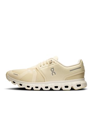 Beige sportssko med mesh-overdel, snørelukning, polstret segmenteret sål og reflekterende detaljer ved hæl og tå.