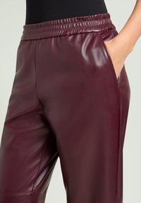 Bordeauxrode nepleren broek met elastische tailleband, voorzien van zijzakken en een soepele textuur, ontworpen voor comfort en draaggemak.