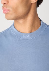 Ανοιχτό γαλάζιο φούτερ με στρογγυλή λαιμόκοψη, που διαθέτει ραμμένες λεπτομέρειες και το λογότυπο "BOSS" στον γιακά, κατασκευασμένο από απαλό και λείο υλικό.