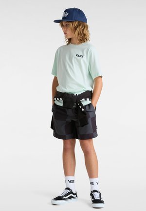 Mintgrünes T-Shirt mit "VANS"-Logo, schwarze und graue gemusterte Shorts, schwarzer Sweatshirt um die Taille gebunden und schwarze Sneakers mit weißen Akzenten.