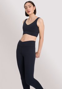 Marineblauwe sport-bh en high-waisted legging gemaakt van rekbare stof. Heeft een V-hals, een naadloos ontwerp en geen zichtbare logo's of patronen.