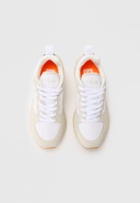 Sustainable sneakers with a white mesh upper, beige suede accents, and orange lining. Features white laces and a gum rubber sole.