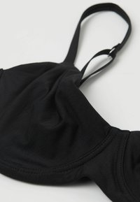 Zwarte bh gemaakt van zacht materiaal. Beschikt over dunne verstelbare bandjes en een glad, naadloos ontwerp zonder zichtbare hardware of versieringen.